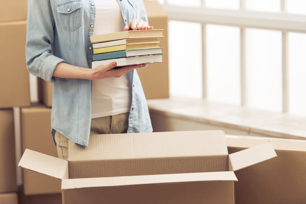 person holding a pile of books over a cardboard box